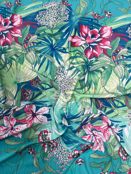 Tropical floral fabric pattern with pink flowers and green leaves on a blue background